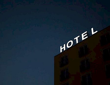 The image shows a building at night with a bright "HOTEL" sign on top against a dark sky.