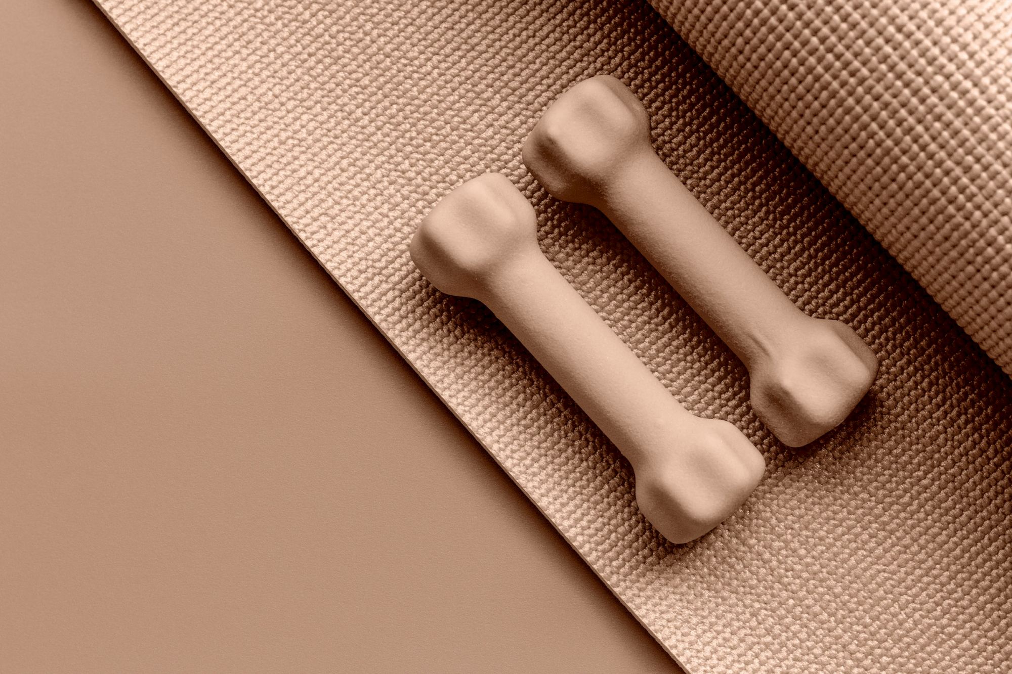 Two beige dumbbells on a textured exercise mat create a coordinated workout setup in minimalist style.