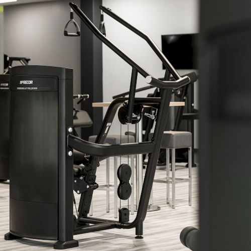 The image shows a gym with various fitness machines, including a seated row machine in a clean, modern space.