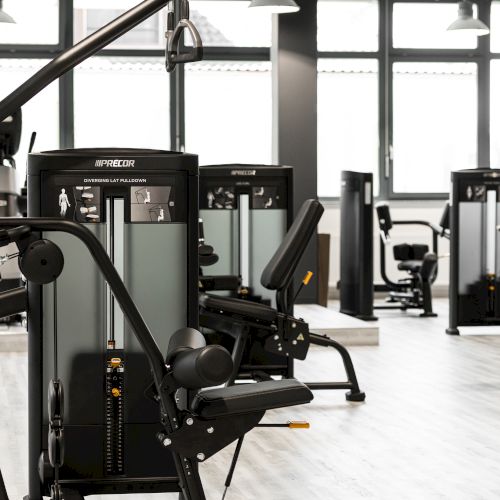 The image shows a modern gym interior with various workout machines and equipment in a bright, spacious setting.