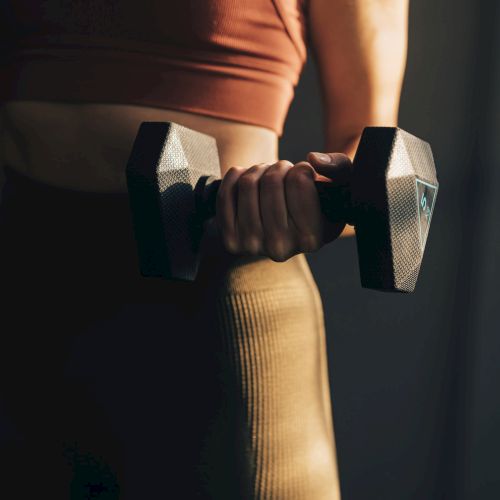 A person holding a dumbbell in one hand, wearing athletic attire, likely engaged in a workout or exercise routine.