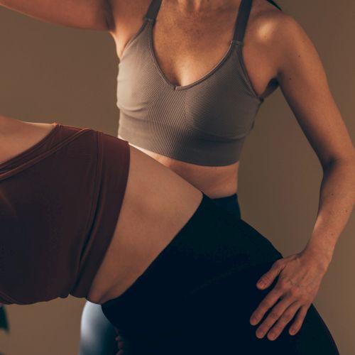 Two individuals practicing yoga or stretching. One person supports the other in a pose, both wearing athletic tops.