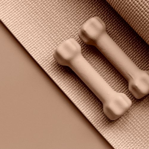 Two light brown dumbbells are placed on a textured exercise mat, all in matching beige tones.
