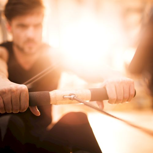 A person is intensely using a rowing machine indoors, with warm light creating an energetic atmosphere.