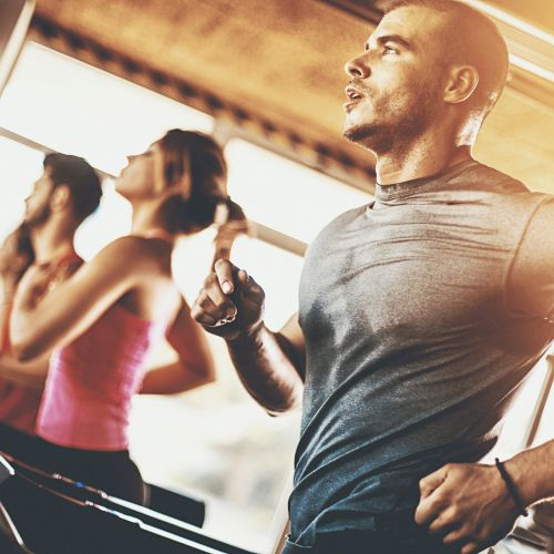 The image shows people exercising on treadmills in a gym, with a focus on a man in the foreground.