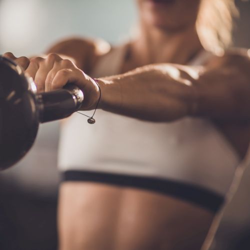A person is shown lifting a kettlebell while working out, wearing a sports bra in a fitness setting.