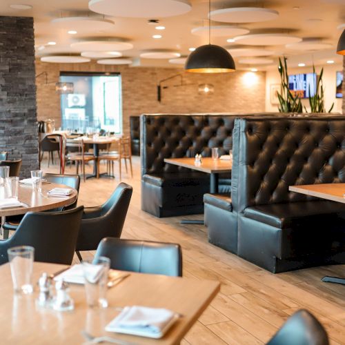 The image shows a modern, empty restaurant with neatly set tables, cushioned booth seating, and stylish lighting fixtures.