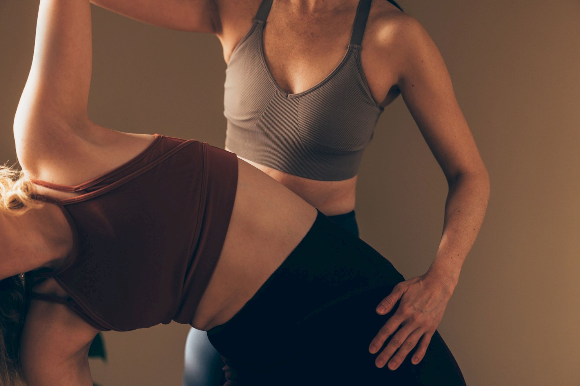 Two people are engaged in a yoga session, with one assisting the other's pose. Both are wearing athletic wear.